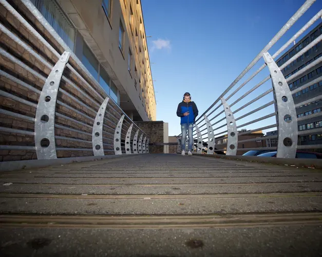 a student walking towards the camera across a bridge