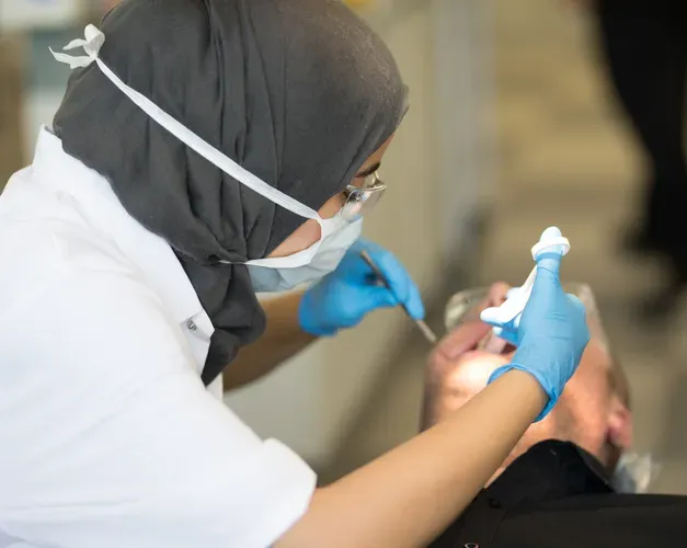 a dental student wearing a mask working on a patients mouth 