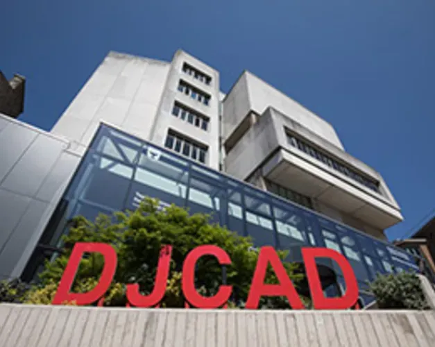DJCAD exterior with a large red sign outside a glass-fronted concrete building under a blue sky
