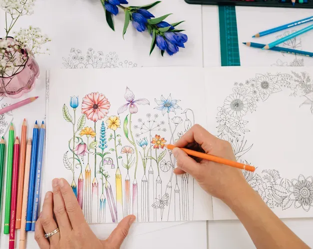 pencils on the left with a persons hand drawing on paper