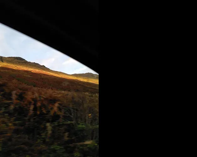 A window frame with a view of a sunlit hill and blue sky