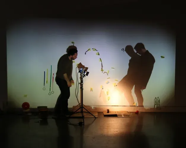 Two people making marks on a projected screen with a light and electrical tape