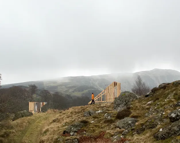 grey skies over rolling hills and two wooden structures facing one another on lower grassy part of hill