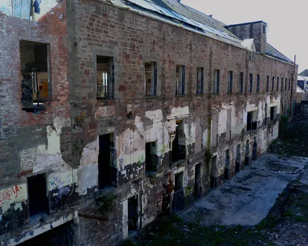 side view of a derelict two story jute mill. Window openings can be seen on the upper and lower levels