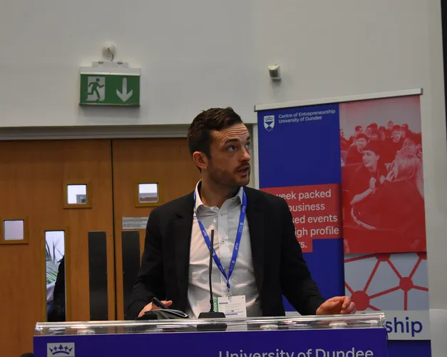 Brian McNicoll standing at a podium with Centre for Entrepreneurship banner at the front presenting at the Venture competition for 2022