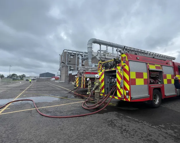 The back of two fire trucjs with water houses leading out and off of the image