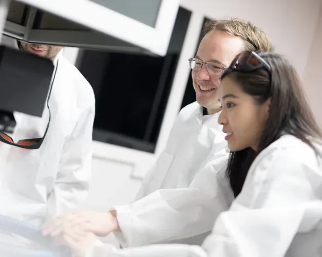 Three people standing over machinery in a lab
