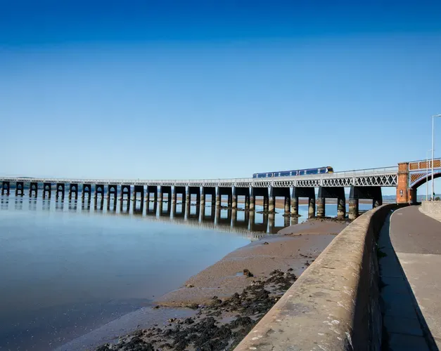 Train crossing bridge over River Tay against bright blue sky