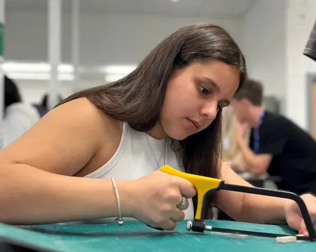 a female secondary school pupil sawing a small piece of wood at the EMBEDD programme