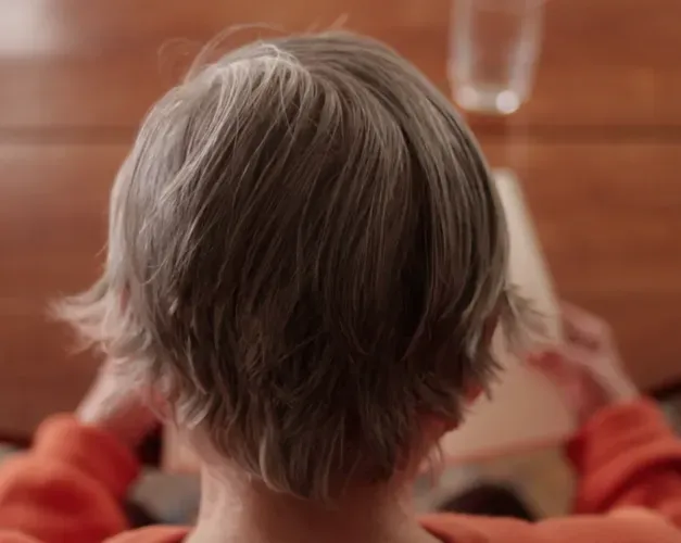 A close up of an elderly woman's head as she reads a book at a table