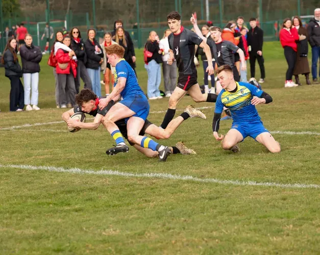 action shot of people playing rugby outside on grass with spectators in background