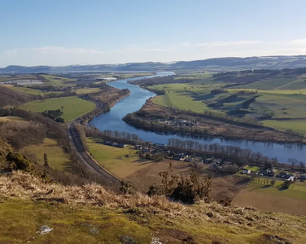 Landcape shot taken high up a hill, showing a river streaming though hills and fields and into the far distance
