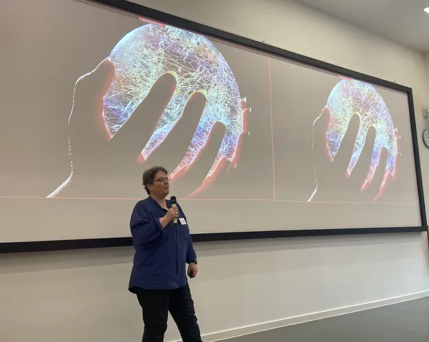 Image of Professor Niamh Nic Daeid presenting in front of an image of a hand holding a round sphere representing a globe which is lit up and full of electronics