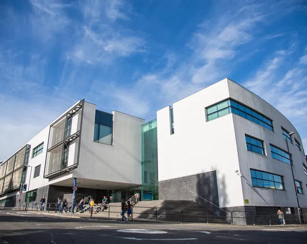 A large white building with blue sky and students walking in the foreground