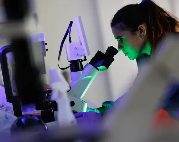 Female scientist in lab coat examining specimen under microscope.