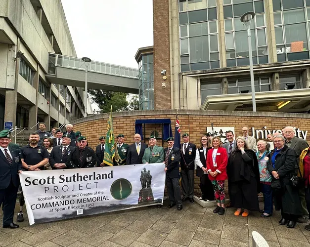 A group of people, some i nkilts and formal wear, holding up a large sign