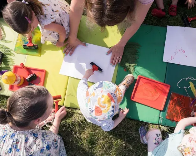 View from above of  young children sitting on grass and painting with their carers