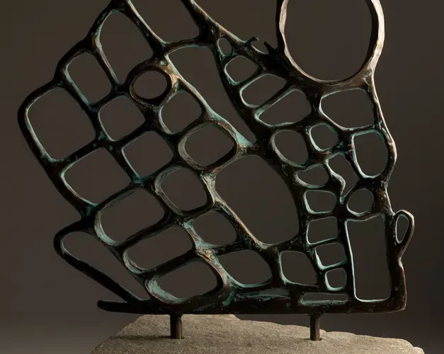 Sculptural metal piece with holes and spikes on a stone pedestal.