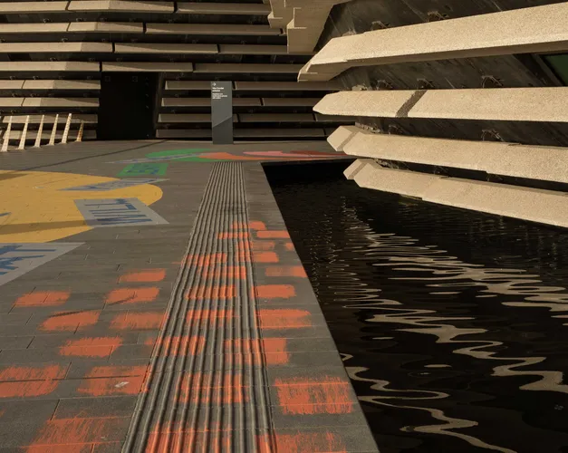 The side of the V&A Dundee building with water below. The pavement has been coloured with bright paints in different patterns.