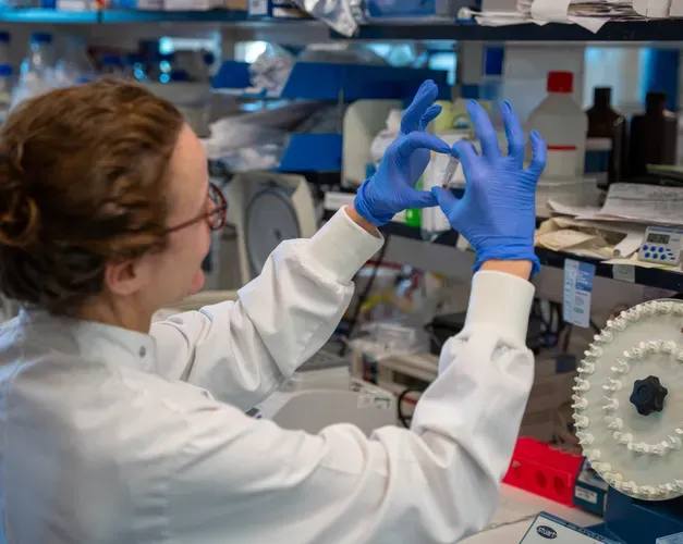 woman in lab wearing a lab coat and blue latex gloves holding up a vile