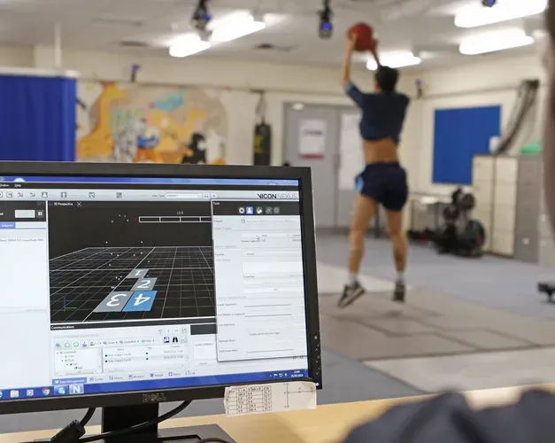 A close shot of a man looking at a computer monitor. Blurred in the background, a man jumps with a ball