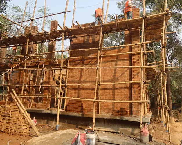 Building with red bricks in the process of being constructed, with scaffolding made from bamboo around it