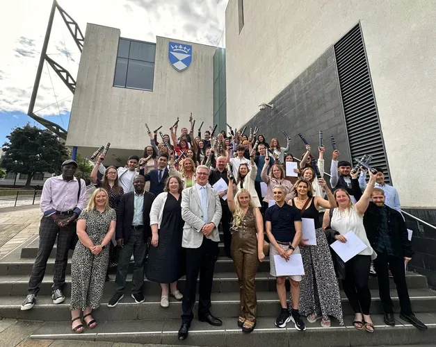 A group of students and academics stand outside the University's Dalhousie Building, on the steps, celebrating after completing Summer School