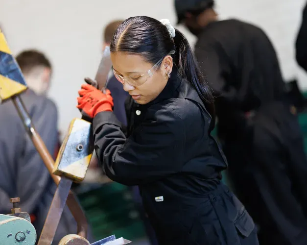 A female student in a boiler suit and gloves operates a piece of industrial equipment