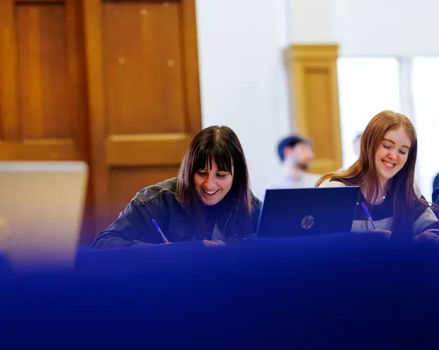 A couple of students sitting side by side taking notes 