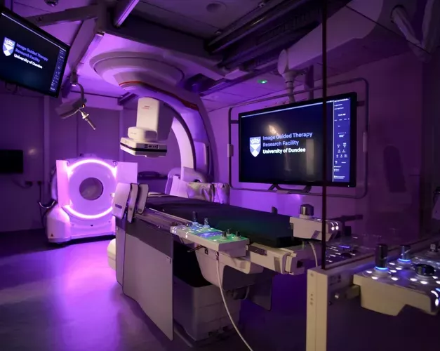 A room featuring a large screen mounted on the wall and medical imaging equipment in the foreground