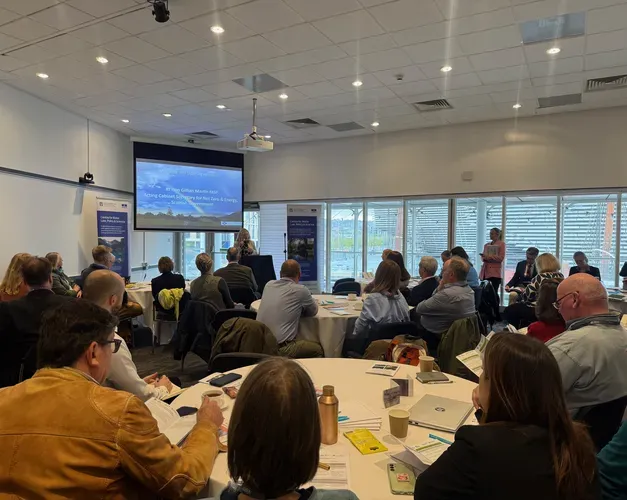 A room full of people sat at tables looking at a presentation