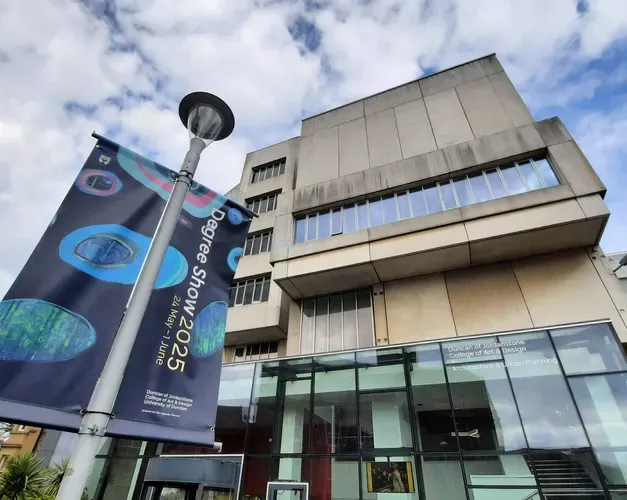 Image of advertising flags hanging from pole outside building, looking upwards at the flags and building