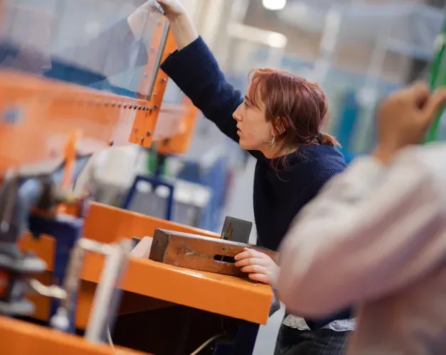 A person leans over a large orange frame, looking through a clear piece of glass.