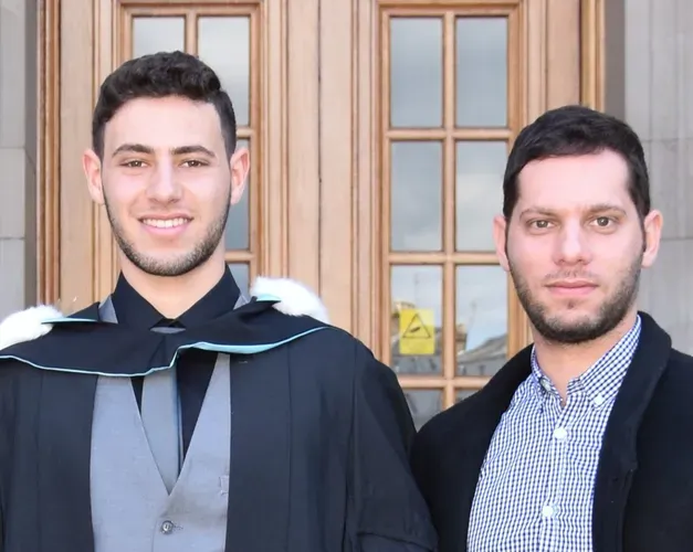two men standing together, one in graduation gown