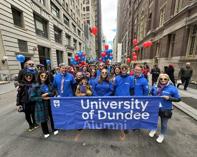 A group of people, standing behind a blue banner that reads University of Dundee pose for a photo