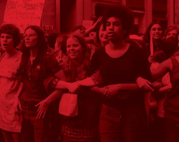 Photograph with red tint. A crowd of women stand linked arm-in-arm at a protest
