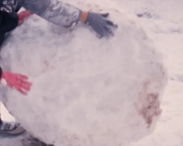 Film still. Gloves rolling a giant snowball