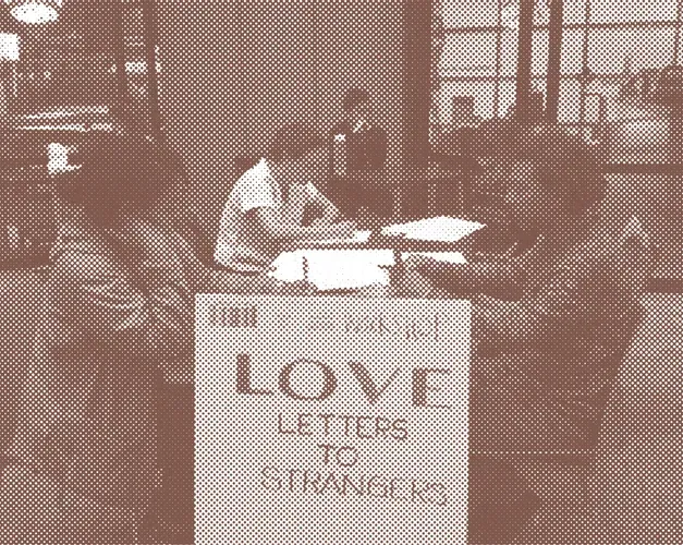 Sepia toned photograph of workshop participants at desks writing. A sign says Love Letters to Strangers