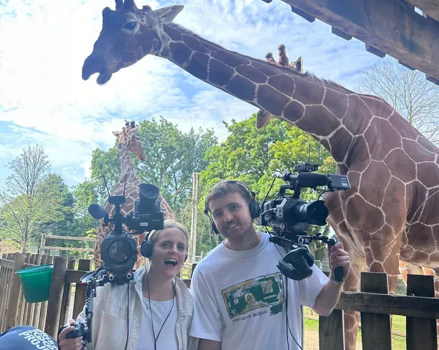 Graduate Euan McClenaghan poses with a colleague and their cameras in front of a giraffe