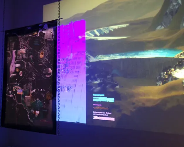 exhibition view, digital projection of a mountain landscape are broken by hanging sheets of textiles and tracing paper