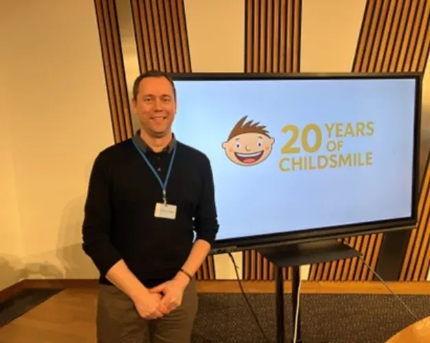 Keith Milburn stands next to the Childsmile logo