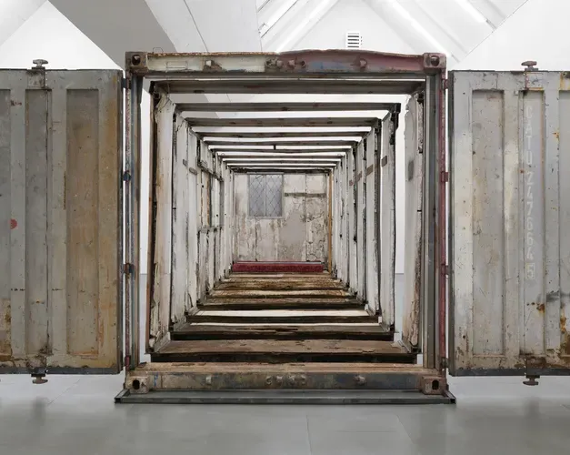 Exhibition view. Tight crop showing the end of a large sculpture. A shipping container cut into sections and laided out in an expanded view