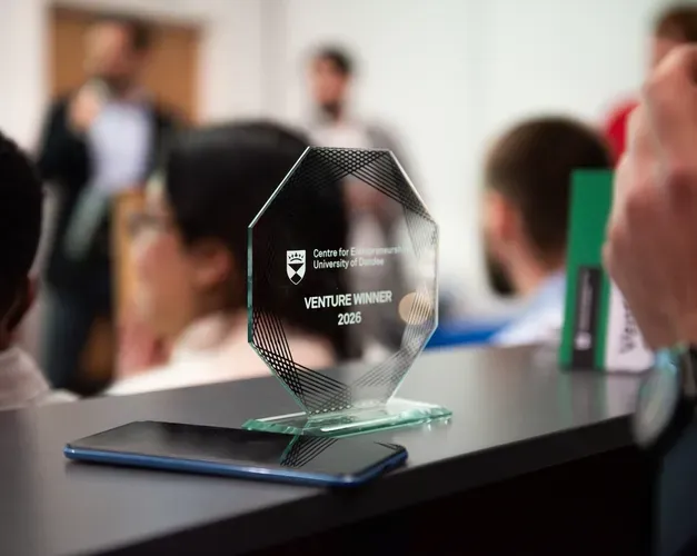 Venture 2026 competition trophy in the foreground with some people blurred out in the room behind it.