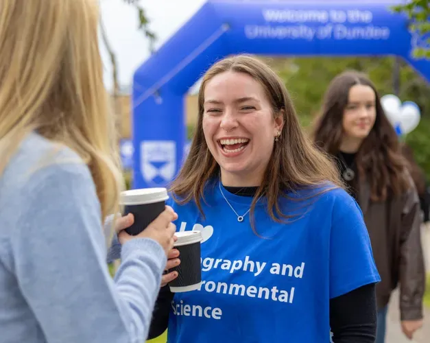 student in blue dundee uni top sharing coffee with friend