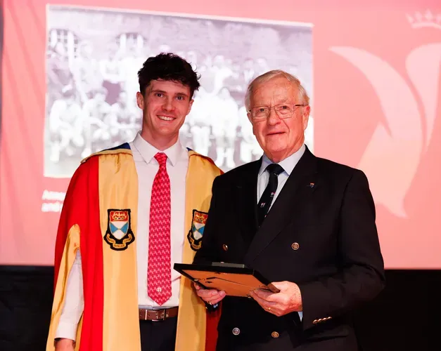 Sports Union presidents Rory La Trobe (2025-26 season) and John Carvell (1967-68 season) stand together at an event. Rory wears the Sports Union President gowns, John wears a suit and holds a framed certificate