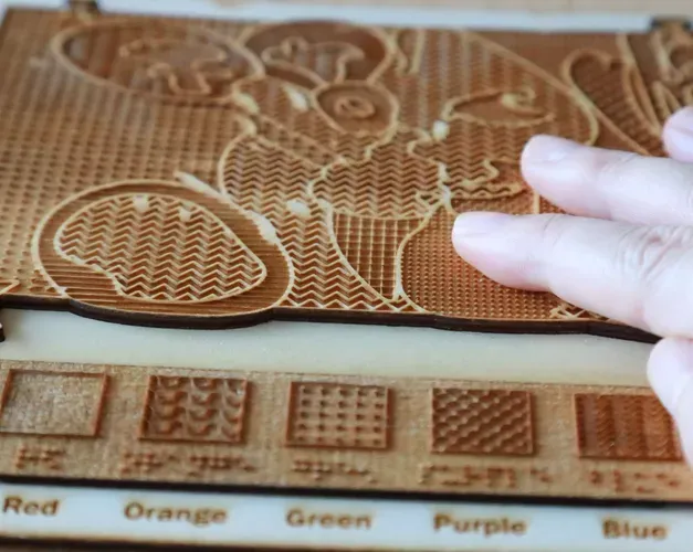 A hand touches a 3D model with raised elements designed to depict the visual appearance and colours of an artwork