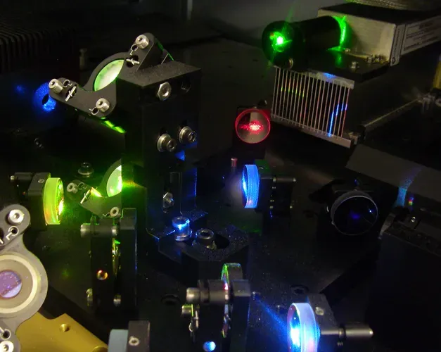 Optical laboratory equipment with green, blue, and red laser beams shining through various lenses and components
