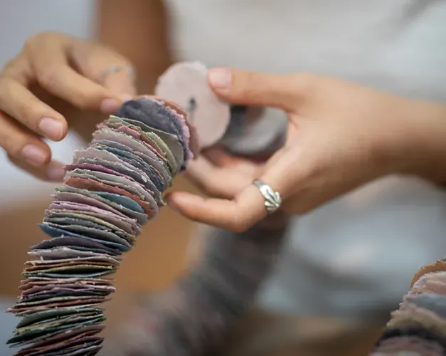 Nayoung's fingers working on several small, ceramic discs which are coloured pink, peach and cream