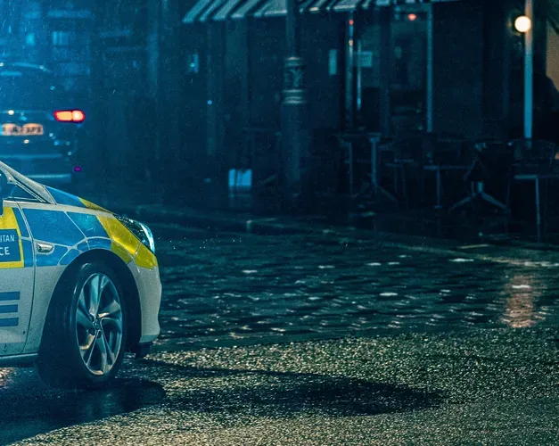 A police car parked at night on a cobbled street