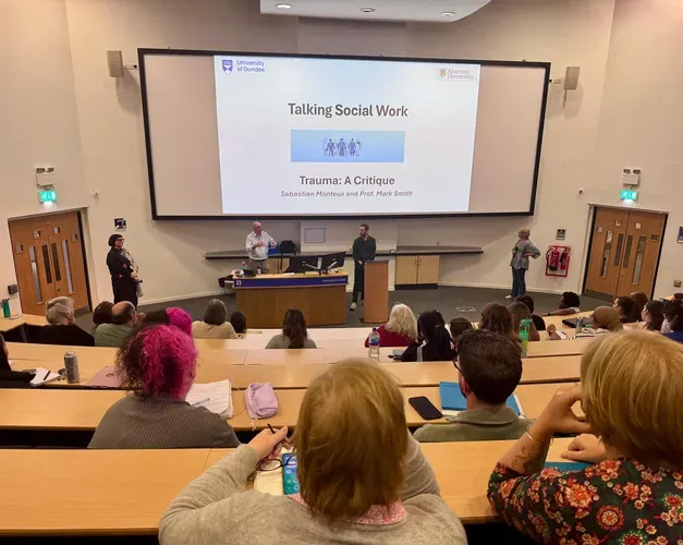 Large lecture theatre with attendees looking at a large screen for an event about Social Work